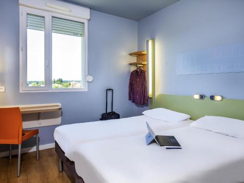 a room with two beds and a desk with a laptop at Ibis Budget Limoges Nord in Limoges