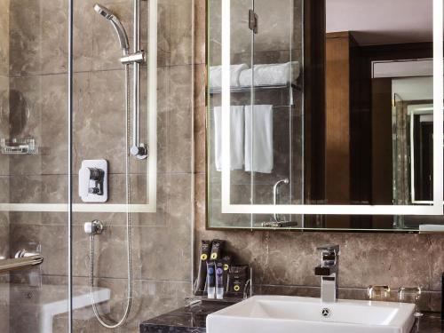 a bathroom with a sink and a shower with a mirror at Novotel Daqing Haofang in Daqing