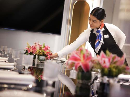 a woman in a kitchen with a table with flowers at Novotel Guwahati GS Road in Guwahati