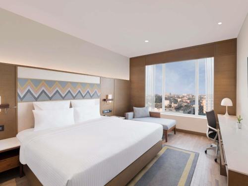 a hotel room with a large white bed and a desk at Novotel Guwahati GS Road in Guwahati