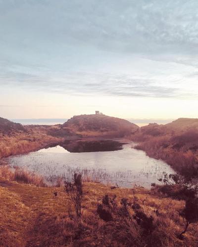 a lake in the middle of a field with a hill at Burwarton cottage in Burwarton