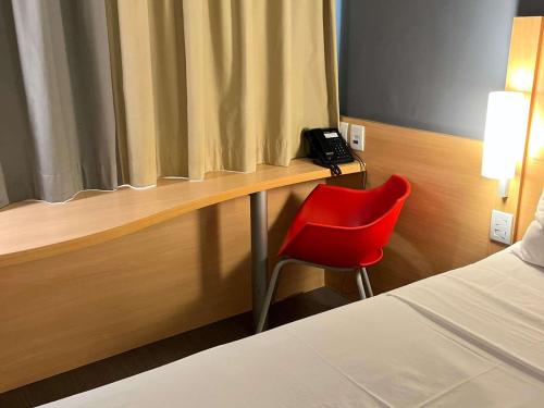 a red chair sitting next to a desk with a phone at ibis Catalao in Catalão
