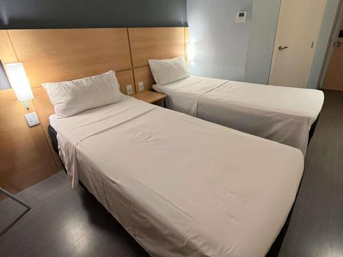 two beds in a hotel room with white sheets at ibis Catalao in Catalão