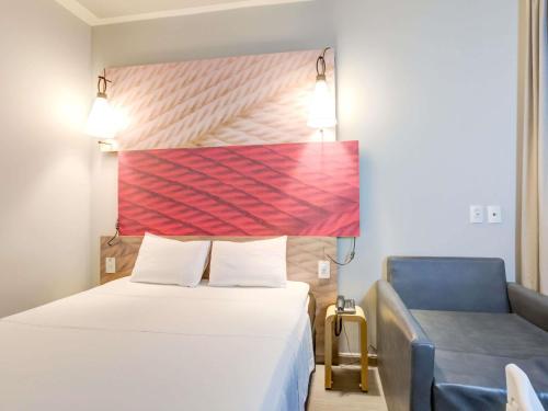 a hotel room with a bed and a blue chair at ibis Paranagua in Paranaguá