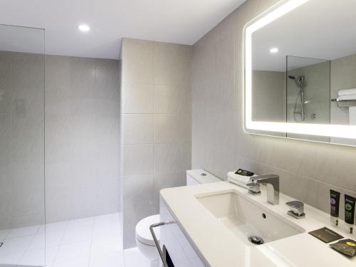 a white bathroom with a sink and a mirror at Novotel Surfers Paradise in Gold Coast