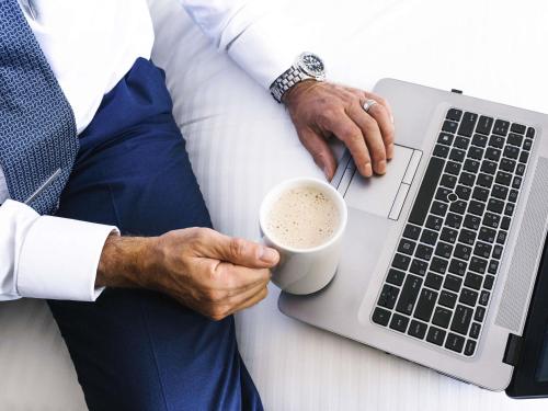 a man in bed holding a cup of coffee and a laptop at Novotel Surfers Paradise in Gold Coast