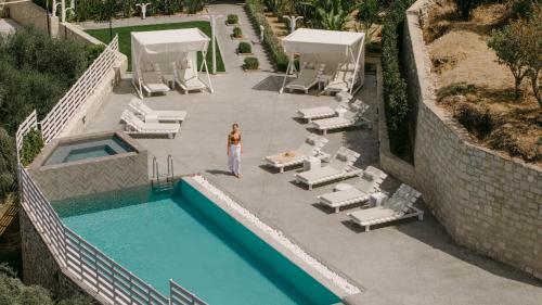 a woman standing next to a swimming pool with lounge chairs at Olivia Villa, Celestial haven of luxury, By ThinkVilla in Perama