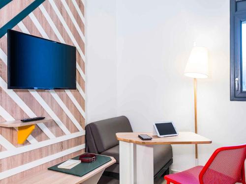 a living room with a table and a tv on a wall at ibis Styles Rouen Val De Reuil in Val de Reuil