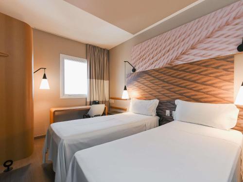 a hotel room with two beds and a window at ibis Jacarei in Jacareí