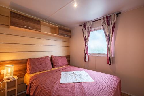 a bedroom with a bed with a red bedspread and a window at Mobil-home Elegance - 3 chambres in Seillac