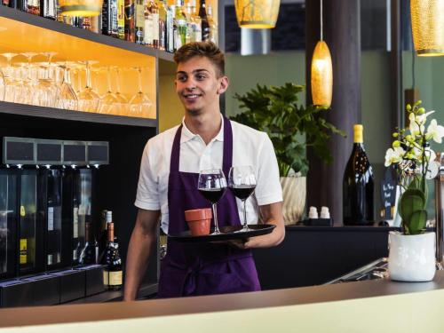 a man in a bar holding a tray of wine glasses at Mercure Blankenberge in Blankenberge