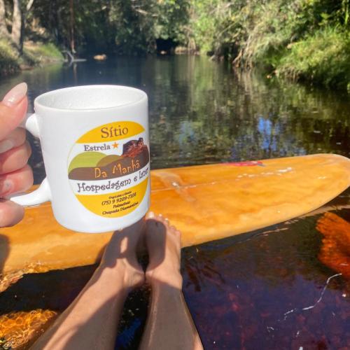 a person holding a coffee cup in front of a river at Sítio Estrela da Manhã Hospedagem e Lazer in Palmeiras