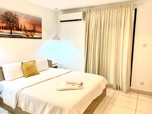 une chambre avec un lit blanc avec un tableau sur le mur dans l'établissement Embassy Gardens Luxury Suites, à Accra
