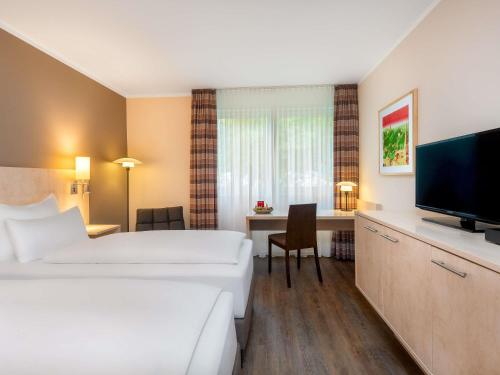 a hotel room with two beds and a flat screen tv at Mercure Hotel Bielefeld Johannisberg in Bielefeld