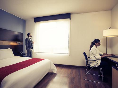 a man and a woman sitting at a desk in a hotel room at Mercure Bogota BH Retiro in Bogotá