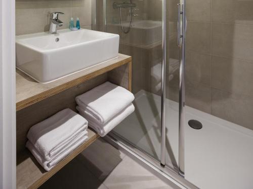 a bathroom with a sink and a shower with towels at ibis Styles Nieuwpoort in Nieuwpoort