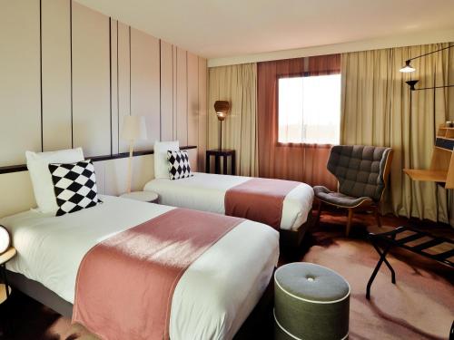 a hotel room with two beds and a chair at Mercure Lyon Genas Eurexpo in Genas