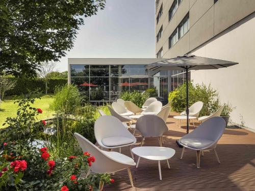 a patio with white chairs and tables and an umbrella at Mercure Lyon Genas Eurexpo in Genas