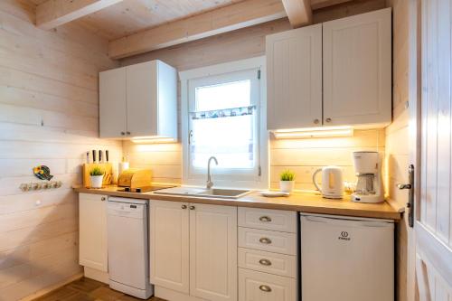 a kitchen with white cabinets and a sink and a window at Domki nad morzem Otulone Słońcem in Rowy