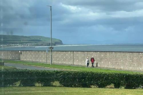 two people walking down a sidewalk next to a brick wall at 4-Bed House - Sea View Garden Parking Wifi in Portstewart
