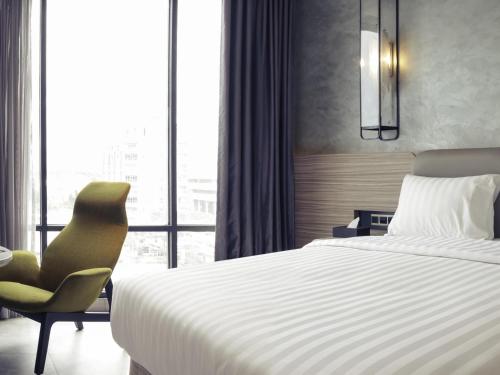 a bedroom with a bed and a chair and a window at Mercure Bandung City Centre in Bandung