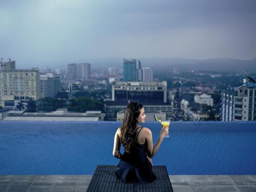 a woman sitting on the edge of a building with a drink at Mercure Bandung City Centre in Bandung