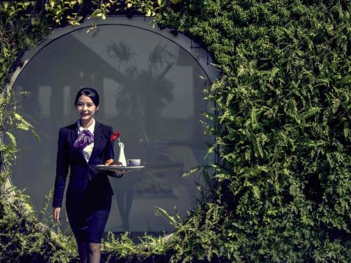 a woman in a suit carrying a tray with a cup of tea at Mercure Bandung City Centre in Bandung