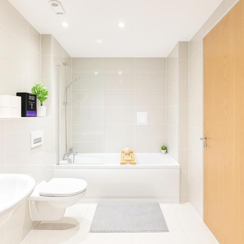 a white bathroom with a toilet and a bath tub at Luxury 2BR Penthouse in Harrow with Balcony, Private Gym, Games Room & Guests Lounge in Harrow
