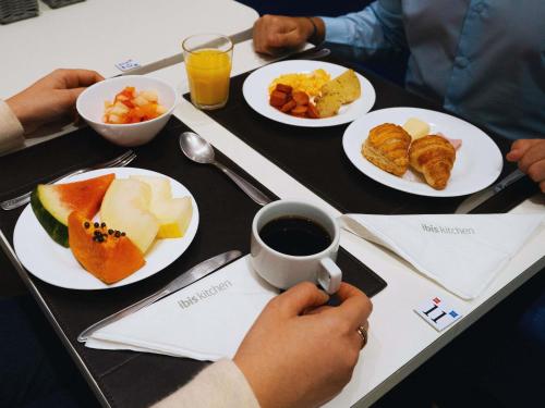 a table with plates of food and a person holding a cup of coffee at ibis Sao Bernardo do Campo in São Bernardo do Campo