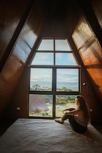 a woman sitting on a bed looking out of a window at VIU Boutique Cabins in San Salvador