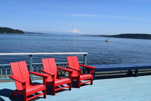 three red chairs sitting on a dock near the water at Sunrise Beach House in Gig Harbor