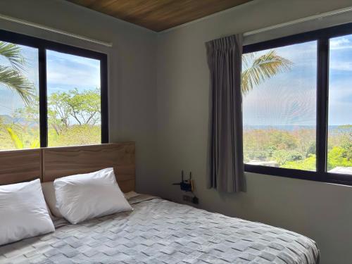 a bedroom with a bed with two pillows and two windows at NulaKai Boutique Apartments in Santa Teresa Beach