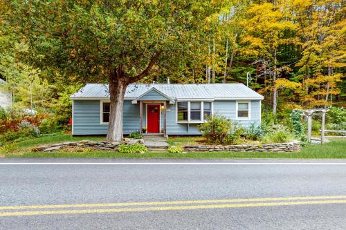 a blue house with a red door and a tree at The River House in West Wardsboro