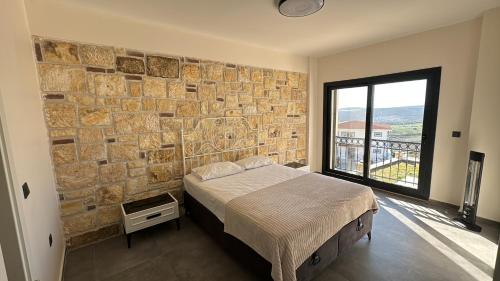 1 dormitorio con pared de piedra, cama y ventana en Foça Taş Villa, en Izmir