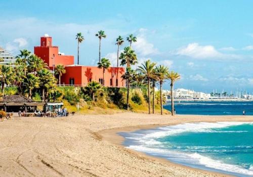 una playa con palmeras y un edificio rojo en Aptos Sol y Playa Benalmádena, en Benalmádena
