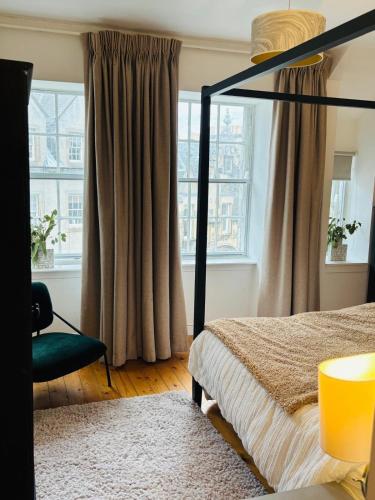 a bedroom with a bed and a chair and windows at Diagon Alley two bed apartment Victoria street grassmarket in Edinburgh