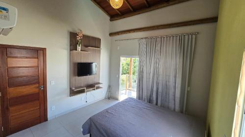 a bedroom with a bed and a tv and a door at Casa Temporada Brisa do Mar in Guriri