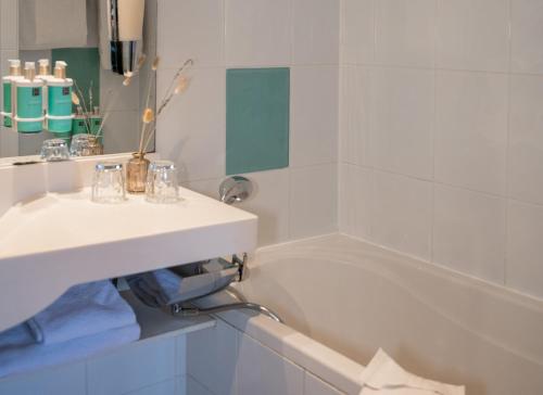 a white bathroom with a sink and a bath tub at Hotel Novotel Domaine de Maffliers - Paris Val-d'Oise in Maffliers