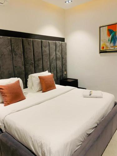 a bedroom with a large bed with white sheets and orange pillows at Alphavista Luxury Apartments in Port Harcourt
