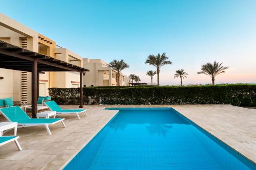 a swimming pool with two blue chairs and a house at Staylish Villas in Joubal Lagoon El Gouna in Hurghada