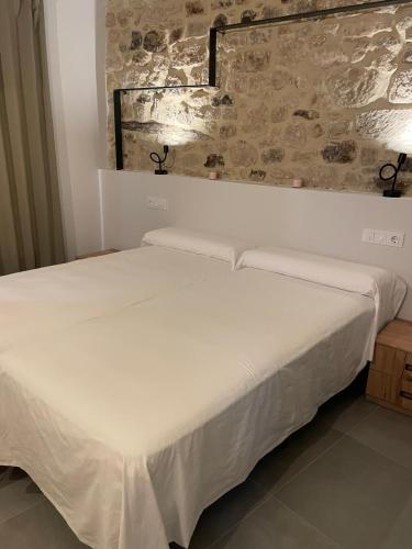 a white bed in a room with a stone wall at Hostal Boutique Restaurante El Algars in Caseras