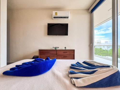 a bedroom with a tv and a bed with blue pillows at Tortuga Azul Private Terrace Rooftop Pool W BBQ Beach Access 11 Pools Free Beach Club in Akumal