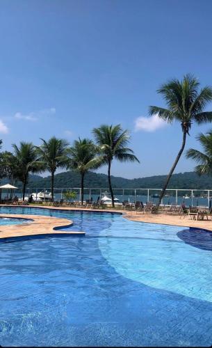 a large swimming pool next to a beach with palm trees at Apart 329 Porto Marina Mont Blanc Refúgio aconchegante com vista privilegiada para a serra, dentro do Hotel in Mangaratiba