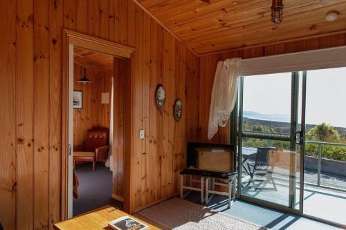 a living room with a television and a sliding glass door at Panorama Cabin - A in Bicheno