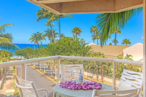 a table with wine glasses and purple flowers on a balcony at Maui Banyan 1 bedroom, ocean view, steps to beach, king-size bed, full kitchen in Wailea