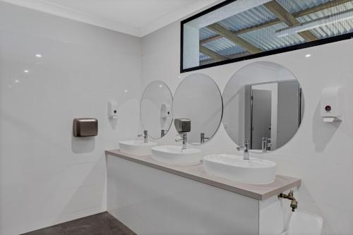 a white bathroom with three sinks and mirrors at Yandina Caravan Park in Yandina