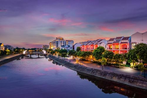 a river with buildings and a bridge at night at Laluna Hoi An Riverside Hotel & Spa in Hoi An