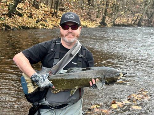 a man holding a large fish in a river at Cozy Three-Bedroom Cabin Near The Salmon River in Altmar, New York in Altmar