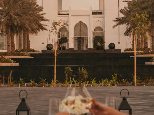 a hand holding a wine glass in front of a building at Raffles Al Areen Palace Bahrain in Manama