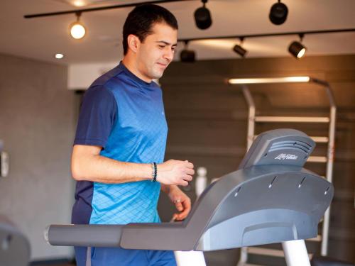 a man standing next to a treadmill in a gym at Novotel Criciuma in Criciúma